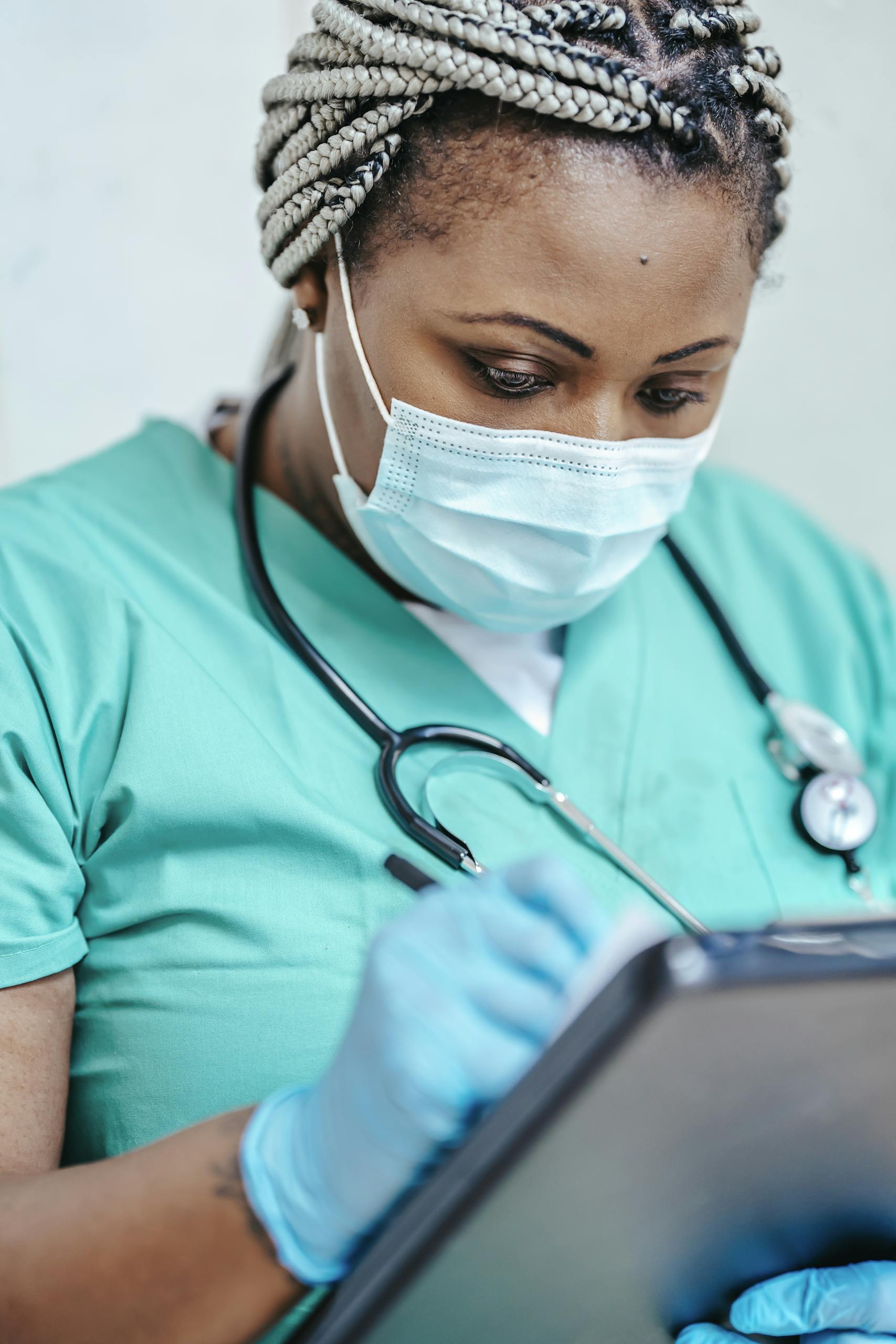 Nurse with mask and gloves reviewing documents on clipboard in a clinic setting.